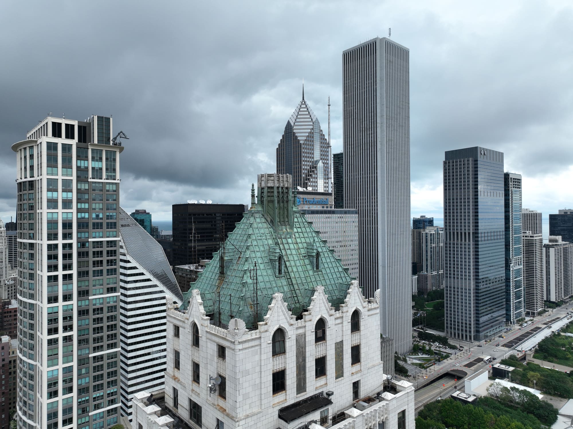 Drone photograph of a gothic terracotta crown and oxidized copper roof in downtown Chicago, surrounded by high-rises under an overcast sky.